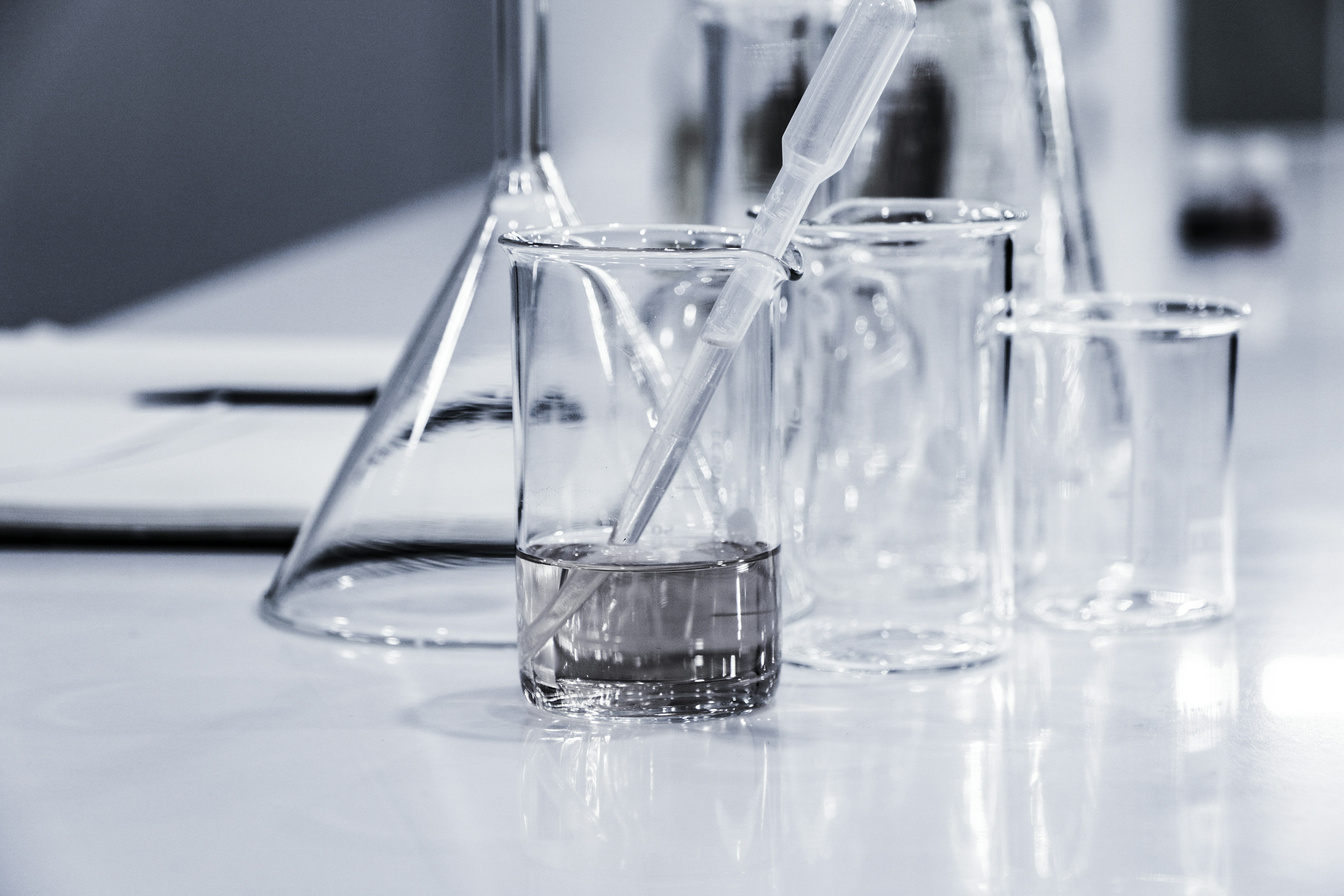 Glass laboratory beakers and pipettes containing clear liquid, representing cosmetic ingredient testing and product formulation.