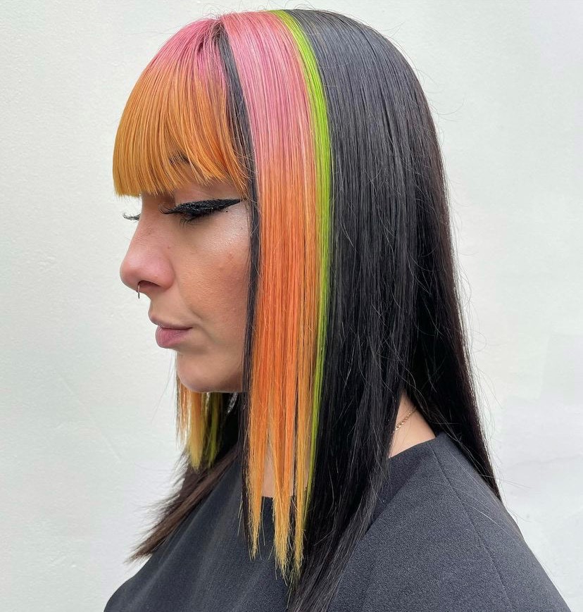 woman with dark hair at the back and rainbow orange, pink and green hair at the front
