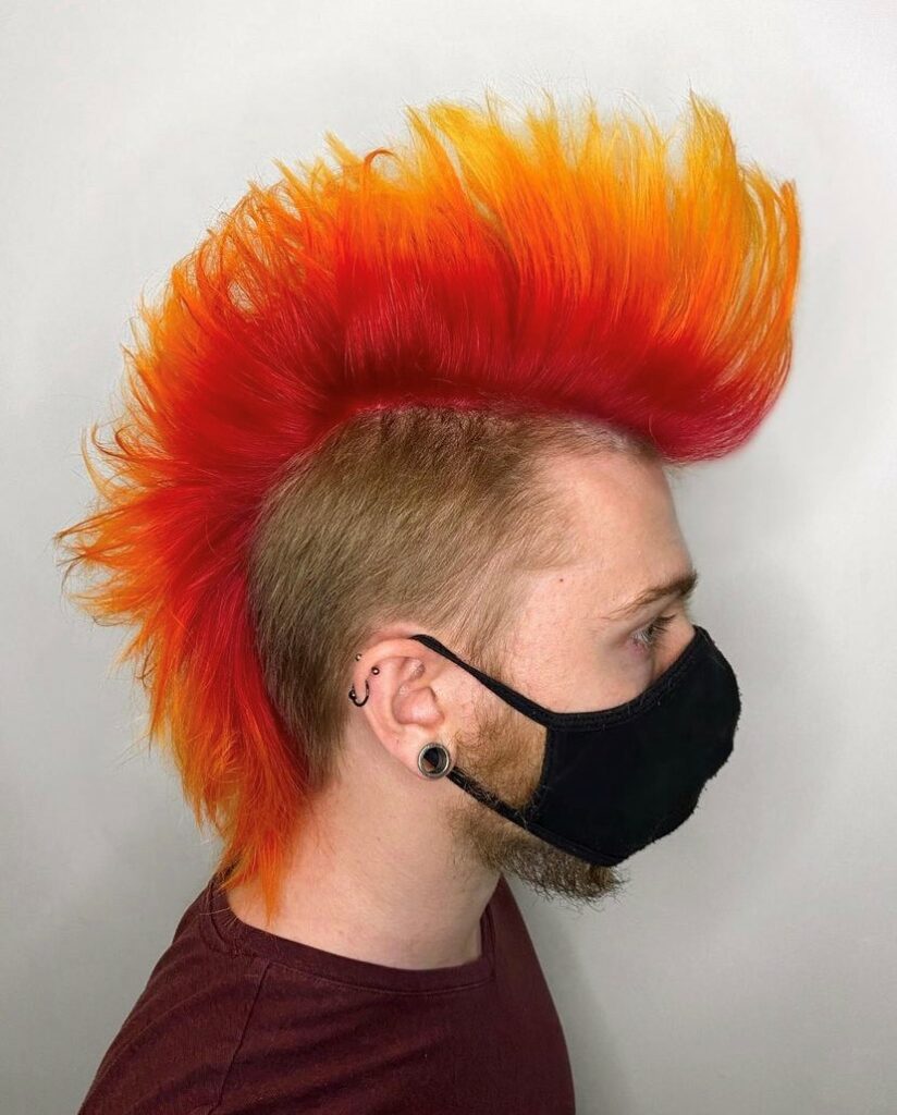 mans side profile wearing a mask with a bright orange ombre mohawk hair style