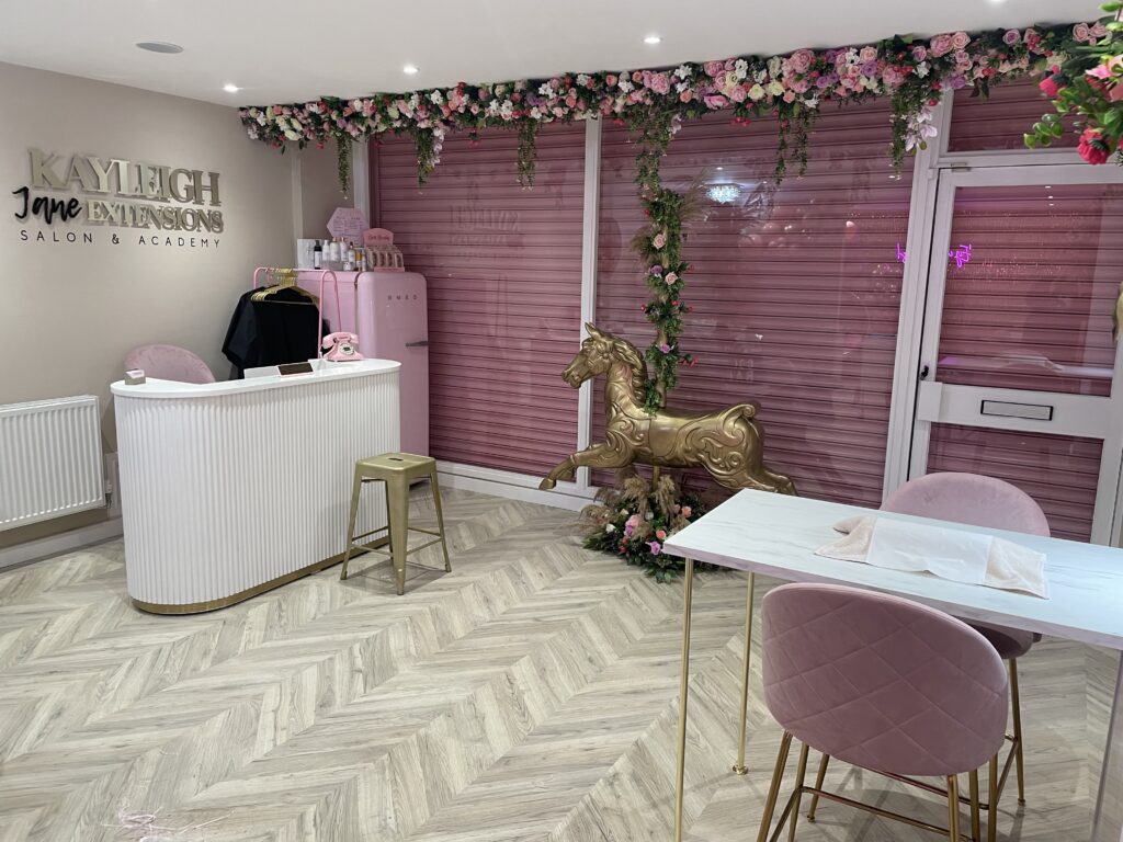 Salon interior showing a nail bar station and front desk. There is a gold rocking horse and floral arrangements