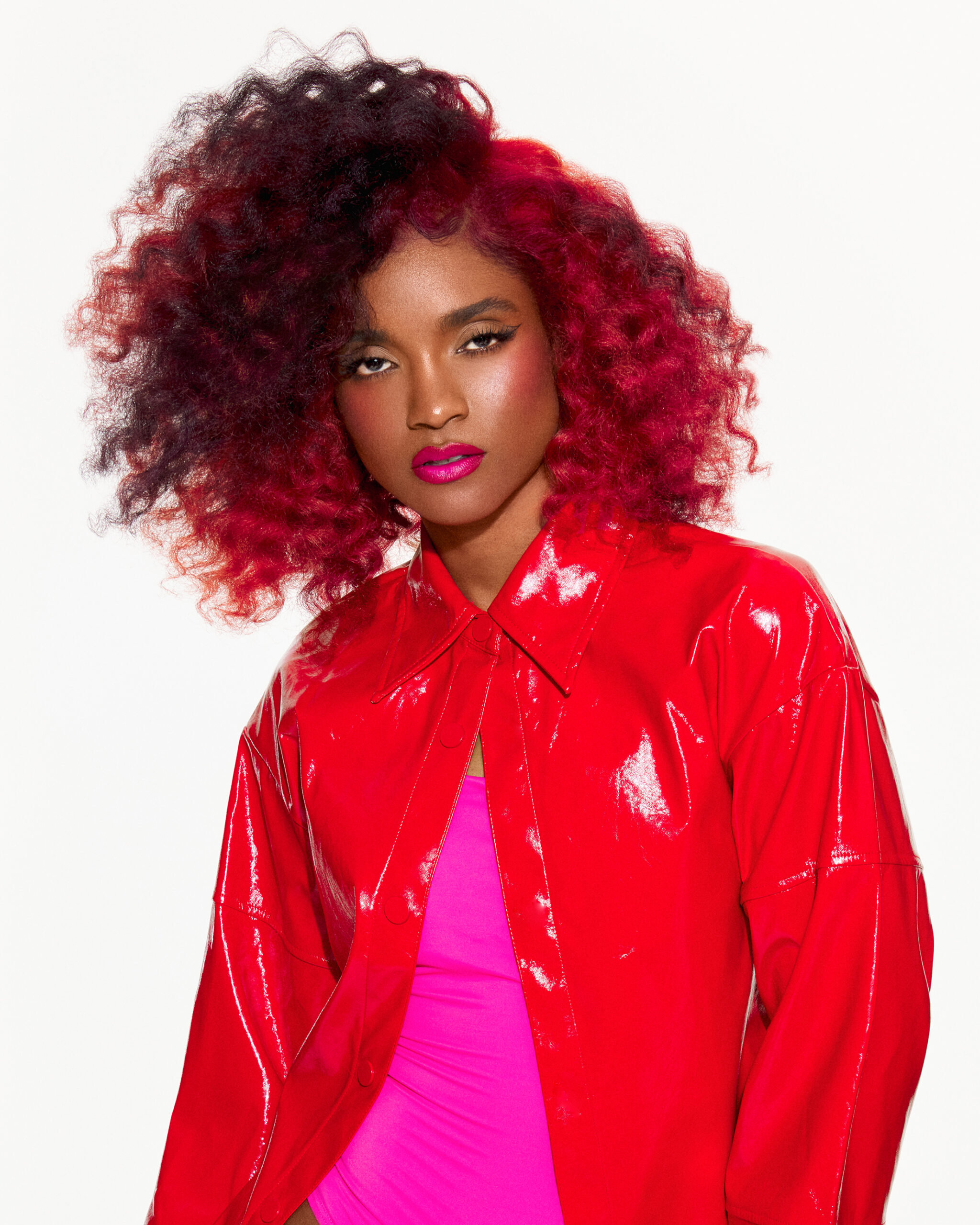 Image of model with curly red hair wearing a red and pink outfit